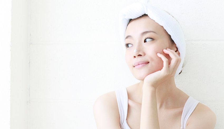 A woman with white face mask on her nose sits with her hand resting on her cheek.